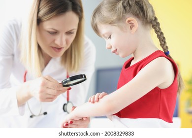 Doctor Pediatrician Examining Rash On Skin Of Hand Of Little Girl Using Magnifying Glass