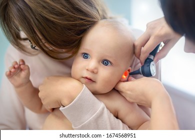 Doctor pediatrist examining childs ear with otoscope. Mom holding baby with hands. Medicine, healthcare ,pediatry and people. Children healthcare and disease prevention concept - Powered by Shutterstock