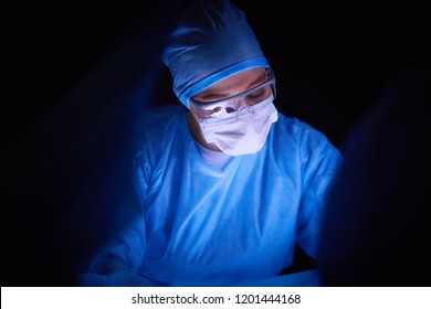 Doctor Performing Surgery In A Dark Background.