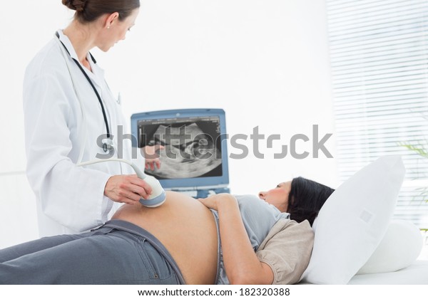 Doctor performing ultrasound on belly of pregnant\
woman in clinic