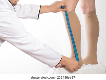 Doctor phlebologist - a vascular surgeon selects the size of the compression stockings of the patient's girl. Measure your feet with a measuring tape. Varicose veins in the legs. White background