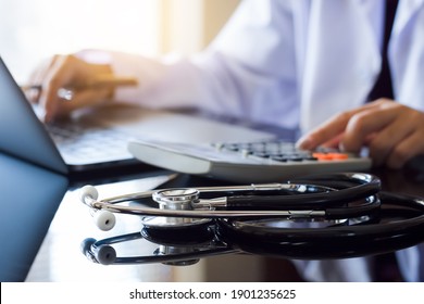 Doctor or physician using calculator and work on laptop computer with medical stethoscope on the desk at clinic or hospital. Medical healthcare costs ,fees and revenue concept.