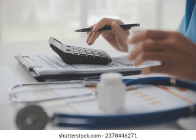 Doctor or physician using calculator and work on laptop computer with medical stethoscope on the desk at clinic or hospital. Medical healthcare costs ,fees and revenue concept. - Powered by Shutterstock