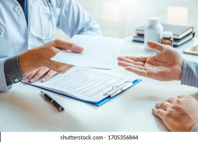 Doctor Or Physician Writing Diagnosis And Giving A Medical Prescription To Male Patient