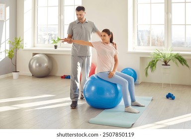 Doctor physiotherapist helping patient do rehabilitation exercises. Man therapist helps happy woman who is sitting on fitness yoga ball do stretching physiotherapy exercises for arms and shoulders - Powered by Shutterstock