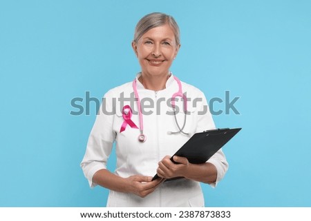 Doctor with pink ribbon, clipboard and stethoscope on light blue background. Breast cancer awareness