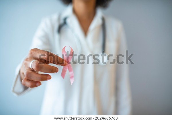 Doctor with pink ribbon and stethoscope on\
white background. Breast cancer awareness. Close up background\
image of unrecognizable female doctor holding pink ribbon as symbol\
of breast cancer\
awareness