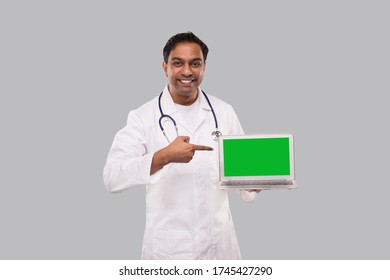 Doctor Pointing At Laptop Green Screen Watching In Camera Isolated. Male Indian Doctor With Laptop In Hands.