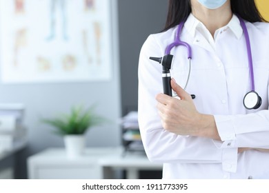 Doctor In Protective Mask Holds An Otoscope In His Hands. Medical Examination At Laura Concept