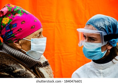 A Doctor In A Protective Mask And Suit Sees Patients During The Coronavirus Pandemic. A Young Girl Doctor In A Medical Mask, Goggles And A Suit Advises A Patient During The Coronavirus Pandemic. 