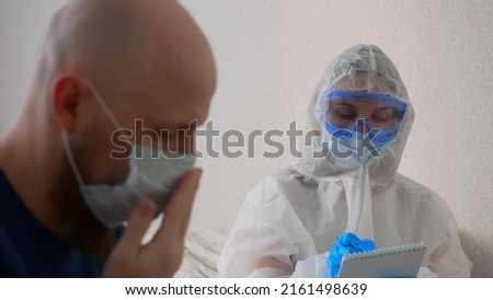 A doctor in a protective suit, mask and goggles writes down the symptoms of the disease. A sick man in a mask complains to the doctor about his well-being, the doctor listens to him carefully. Stock photo © 