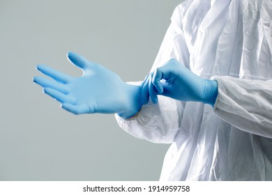 Doctor in a protective suit puts on blue rubber gloves