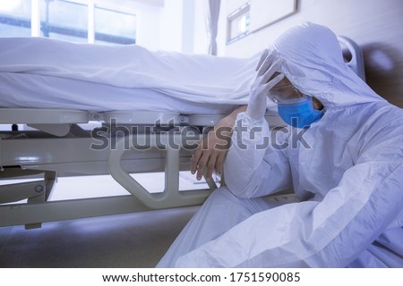 Doctor in protective suit, sadness and depressed beside Coronavirus victim body on bed after the death of patient.