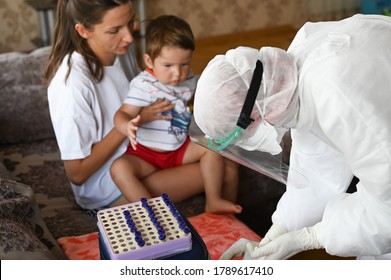 A Doctor In A Protective Suit Takes A Blood Test From A Child At Home