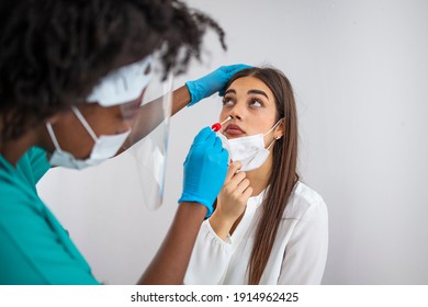 Doctor in protective workwear taking nose swab test from young woman. Close-up of woman having PCR testing at the hospital. Woman being screened for coronavirus in a laboratory
