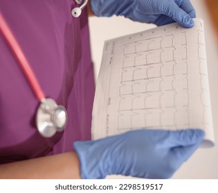Doctor doctor in a purple coat, with a stethoscope and gloves looking at the results of ecg tests