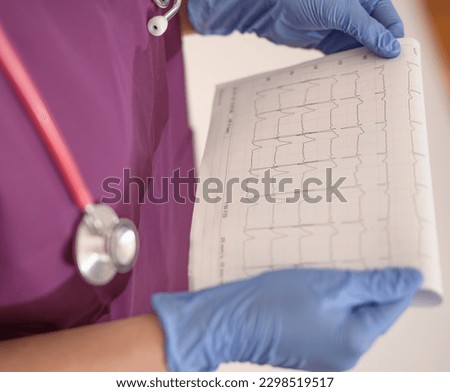 Doctor doctor in a purple coat, with a stethoscope and gloves looking at the results of ecg tests