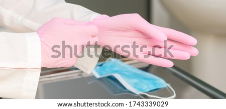 Doctor puts on pink latex gloves in hospital close up.