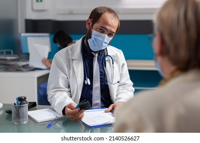 Doctor Putting Medical Seal On Prescription Paper, Giving Medicine To Senior Patient At Examination. General Practitioner Using Stamp On Consultation Report During Covid 19 Pandemic.