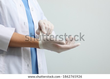 Doctor putting on medical gloves against light grey background, closeup