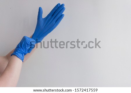 Doctor putting on protective blue gloves on white background