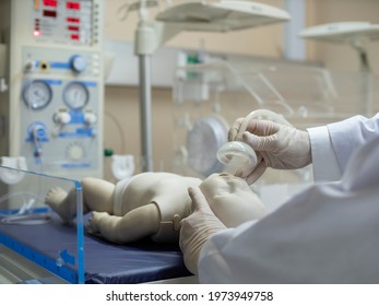 A Doctor Putting An Oxygen Mask On A Newborn Infant Model Under A Radiant Warmer Resuscitator Unit. Neonatal Care Concept. Sick Children Concept.