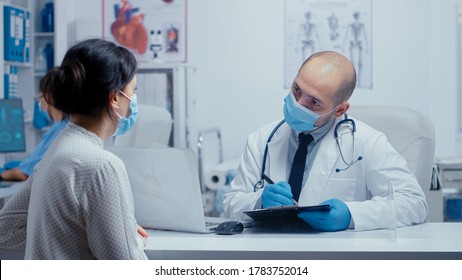 Doctor Questioning Patient During Covid-19 Pandemic, Writing Answears In Clipboard. Medical Consultation In Protective Equipment Concept Shot Of Sars-cov-2 Global Health Pandemic Crisis