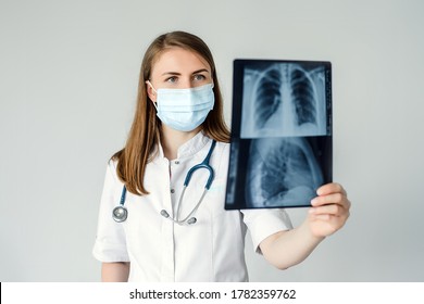 Doctor Radiologist Look Learn Waych Human Skeleton Of Lungs. A Woman In A White Coat With A Mask And Stethoscope On Her Neck Is Studying Fluorography.