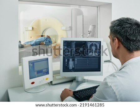 Doctor radiologist running CT scan for patient's body lungs from control room. Computed Tomography