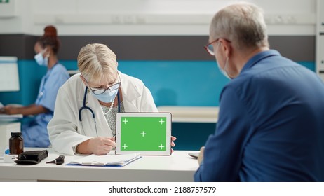 Doctor And Retired Person Looking At Greenscreen On Tablet During Covid 19 Pandemic In Medical Cabinet. Blank Mockup Background With Isolated Copyspace And Chroma Key Template.