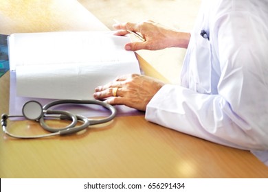 Doctor Is Reviewing Patient Health History Data From File At Doctor Office In Hospital With Stethoscope On The Table