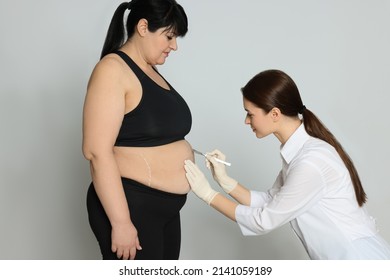 Doctor with scalpel near obese woman on light background. Weight loss surgery
