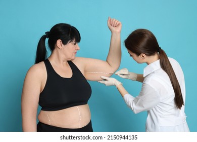 Doctor With Scalpel Near Obese Woman On Light Blue Background. Weight Loss Surgery