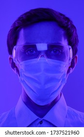 Doctor Or Scientist With Glasses And A Medical Mask. Portrait In A Dramatic Blue-violet Neon Light.