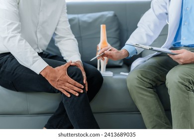 Doctor is seeing a patient. sitting and holding his knees with discomfort Meanwhile, bone model. talking about knee pain or osteoarthritis. - Powered by Shutterstock