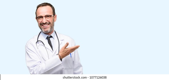 Doctor senior man, medical professional holding something in empty hand isolated over blue background