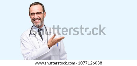 Doctor senior man, medical professional holding something in empty hand isolated over blue background