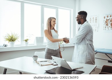 Doctor shaking hands with woman. Female patient visiting health professional. They are in hospital. Cropped shot of a handsome young male doctor and his patient shaking hands in the hospital - Powered by Shutterstock