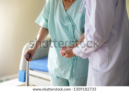 The doctor shook hands, encouraged and supported the patient, Which holds a cane to help support in the hospital, to healthy and health insurance concept.