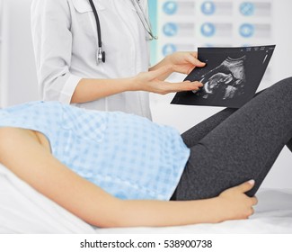 Doctor showing baby ultrasound image to pregnant woman