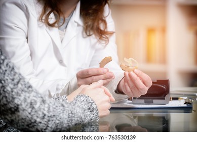 Doctor Showing Hearing Aid To Her Patient In The Doctor's Office