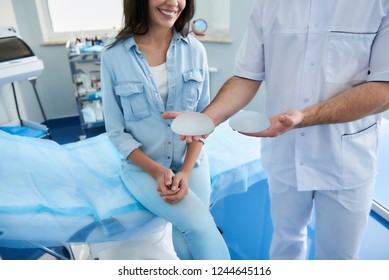 Doctor showing options for silicone implants for happy female patient in beauty clinic