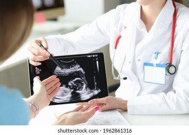 Doctor showing patient woman ultrasound scan of fetus on digital tablet closeup