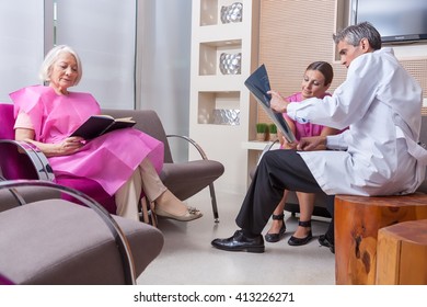 Doctor Showing Patient X-ray Scan In Hospital Waiting Room.