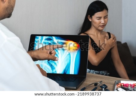 Doctor showing a x-ray of pain in the shoulder on a laptop. Woman patient holding her shoulder
