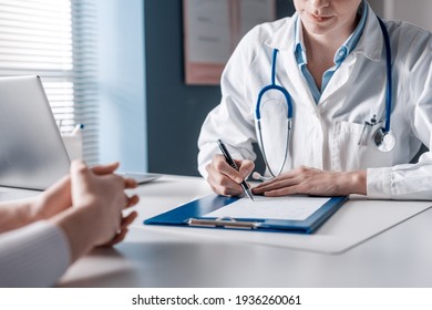 Doktor sitzt am Schreibtisch und schreibt für ihre Patientin ein Rezept