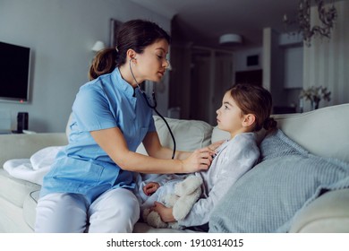 Doctor sitting on sofa next to girl and examining her lungs with stethoscope. Doctor at home service.