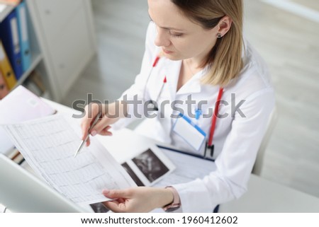 Doctor sitting at table and looking at cardiogram in clinic