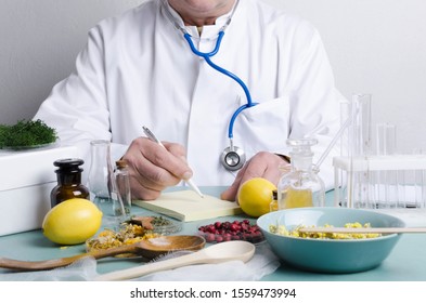 Doctor Sitting At The Table. Many Ingredients For Alternative Medicine.Dried Berries,herbs,lemons And Diffirent Portions Of Natural Medicines On The Blue Table