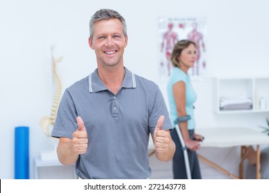 Doctor smiling at camera while his patient standing with crutch in medical office - Powered by Shutterstock